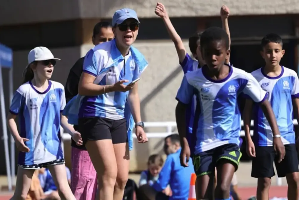 Enfants de l'école d'athlétisme de l'OM et leur éducatrice, bras levés, au stade
