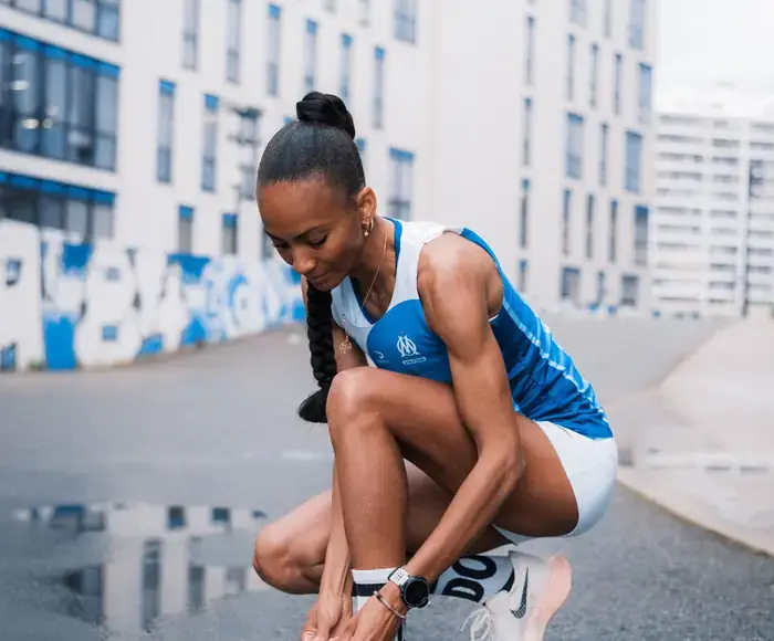 Athlète de l'OM Athlétisme en tenue officielle, laçant ses chaussures